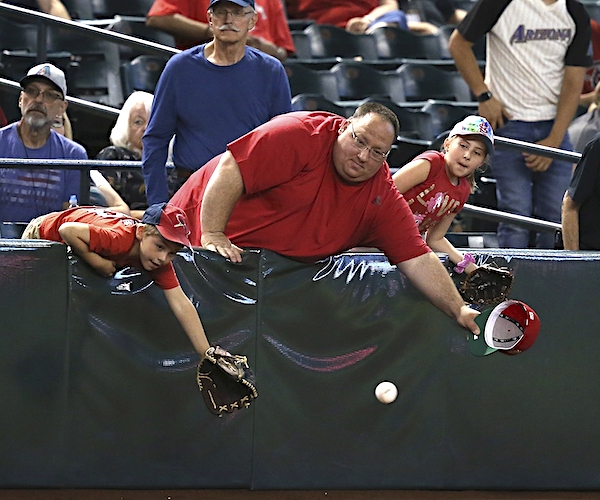 a father and his son lean over the railing to try to catch a souvenir baseball