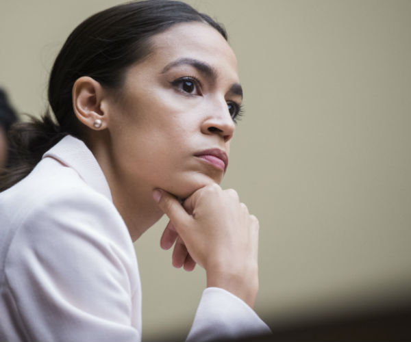 Alexandria Ocasio-Cortez is shown in a white suit, at a house oversight and reform committee meeting