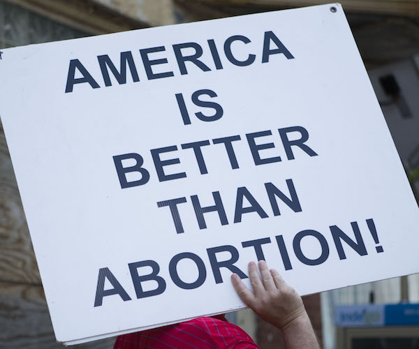 pro life protesters hold up a sign that reads america is better than abortion