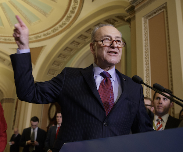 chuck schumer points in the air with his right hand while delivering remarks to reporters